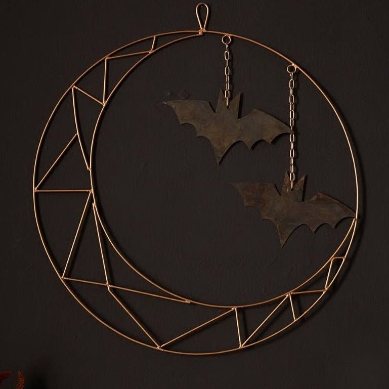 A metal wreath with a geometric crescent shape and hanging bats, intended for wall or door decoration.
