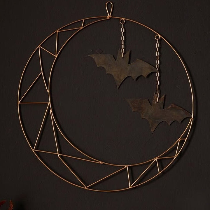 A metal wreath with a geometric crescent shape and hanging bats, intended for wall or door decoration.